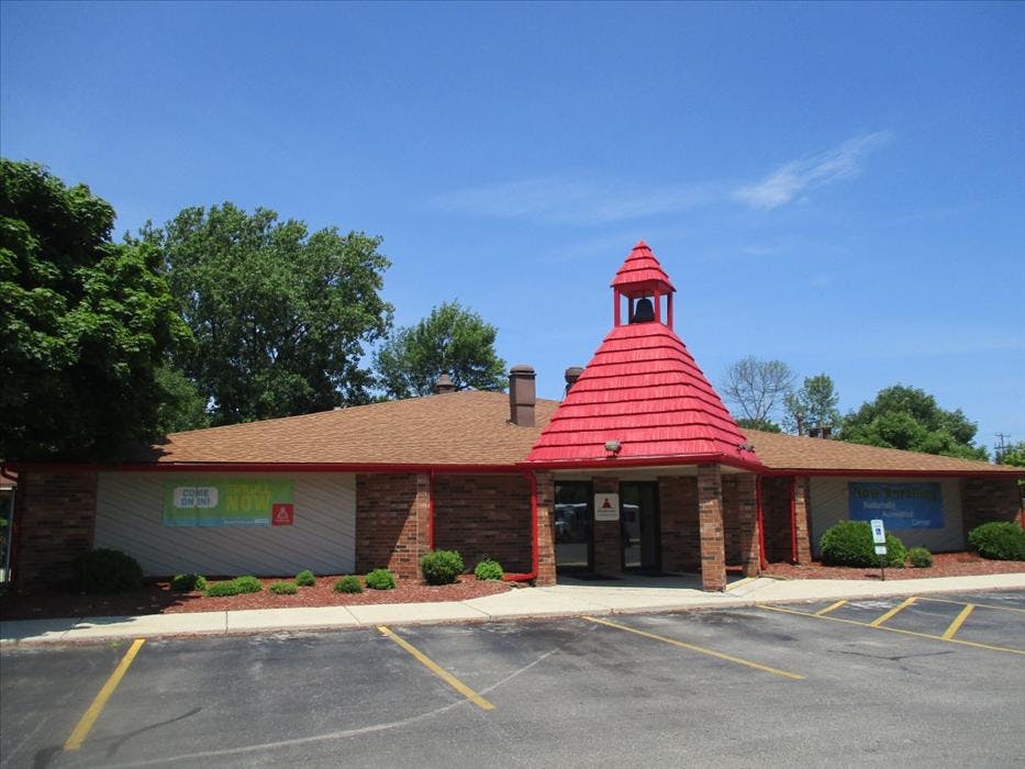 Building with a red bell tower entrance, brown roof, and parking lot
