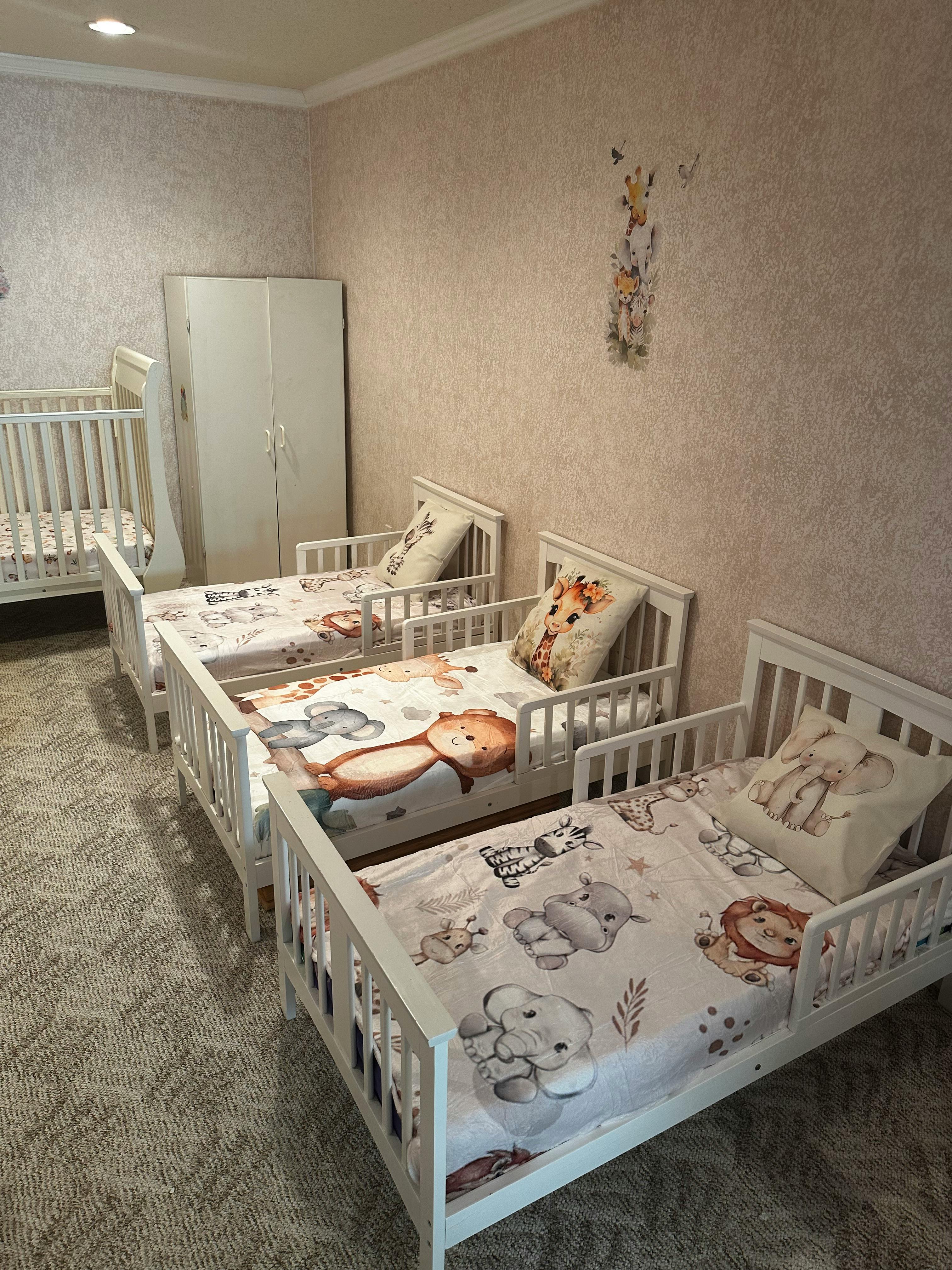 Multiple white toddler beds with animal-themed bedding in a room