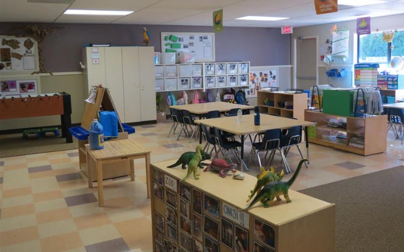 Classroom with tables, chairs, storage cubbies, and dinosaur toys