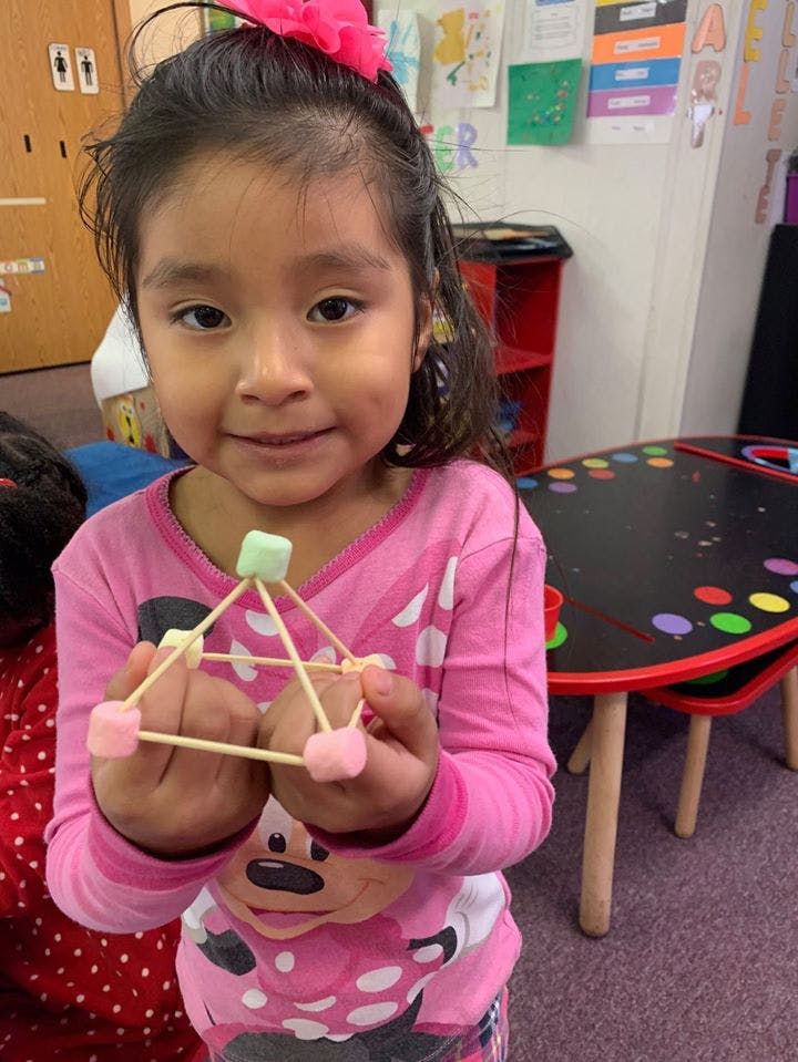 Child holding a structure made of toothpicks and marshmallows