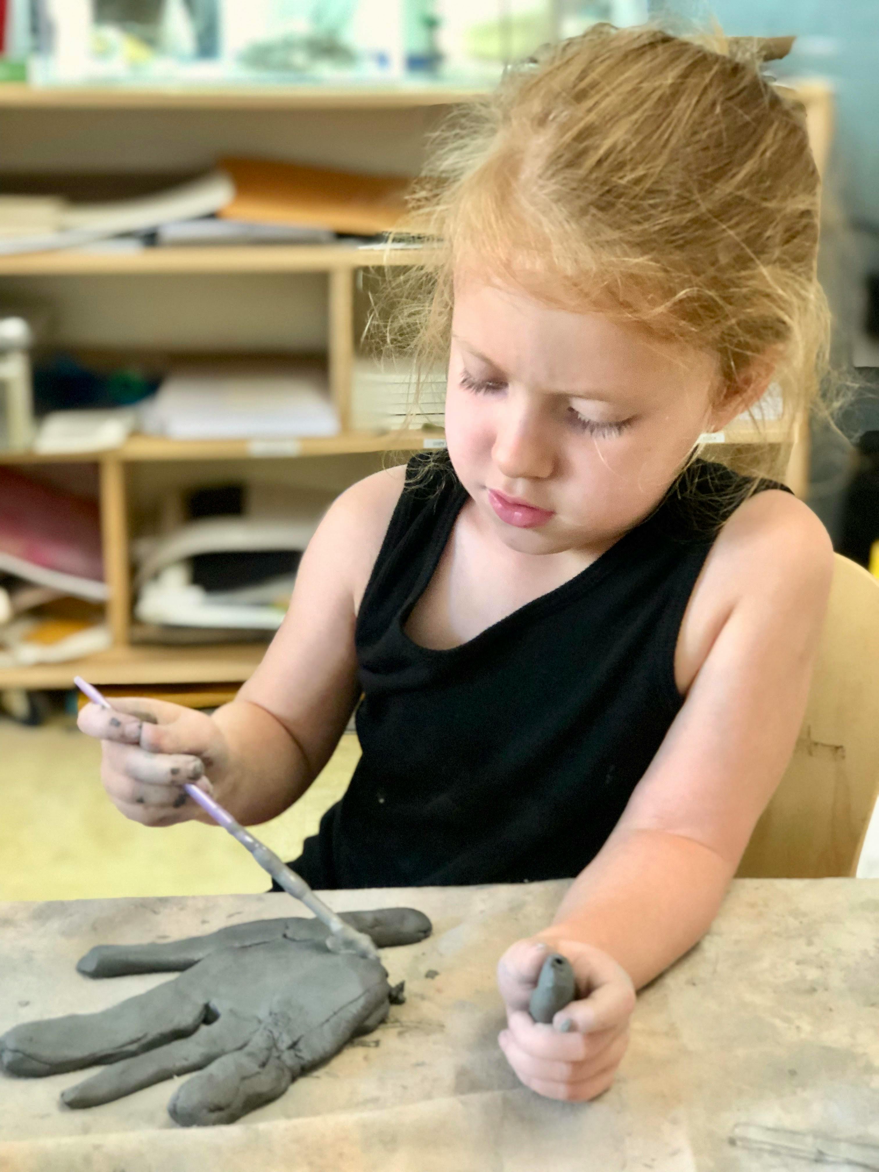 Child sculpting clay hand with a tool