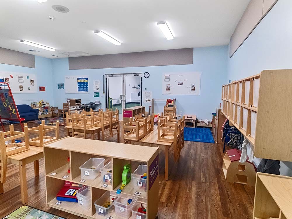 Empty classroom with small tables and chairs, storage units, and whiteboard displays