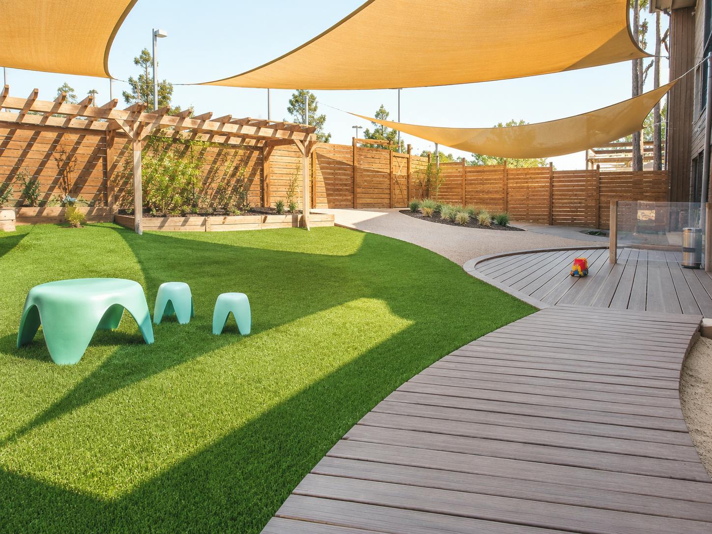 Outdoor play area with synthetic grass, wooden deck, and overhead sun shades