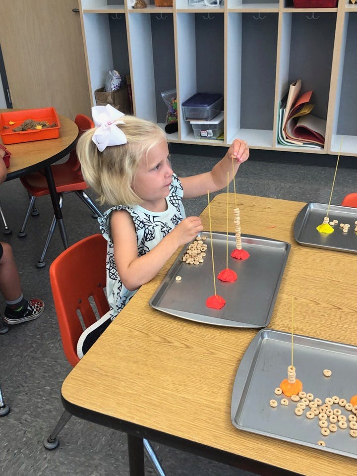 Child stringing cereal onto spaghetti noodles in a classroom