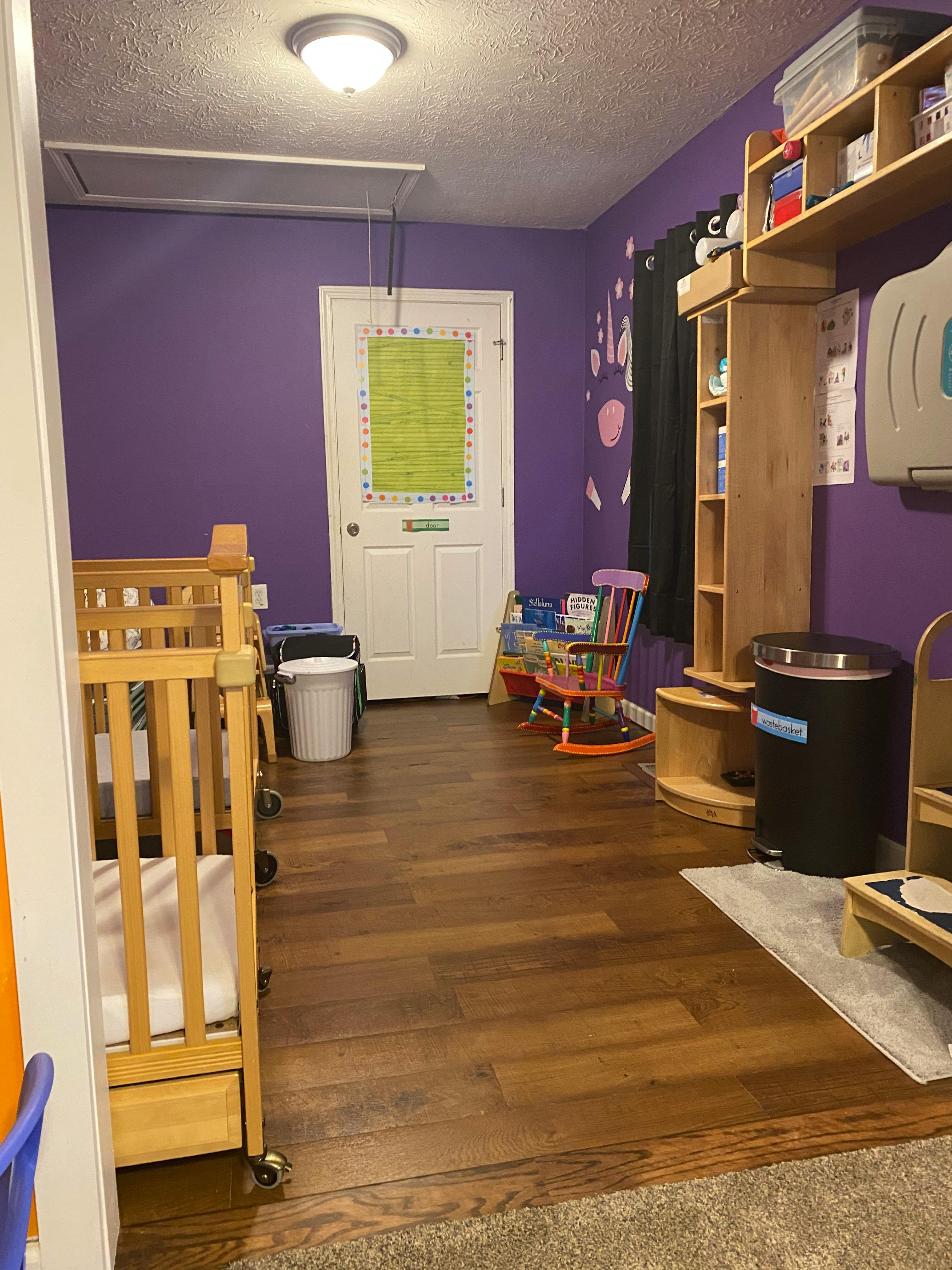 Nursery room with cribs, purple walls, and a white door