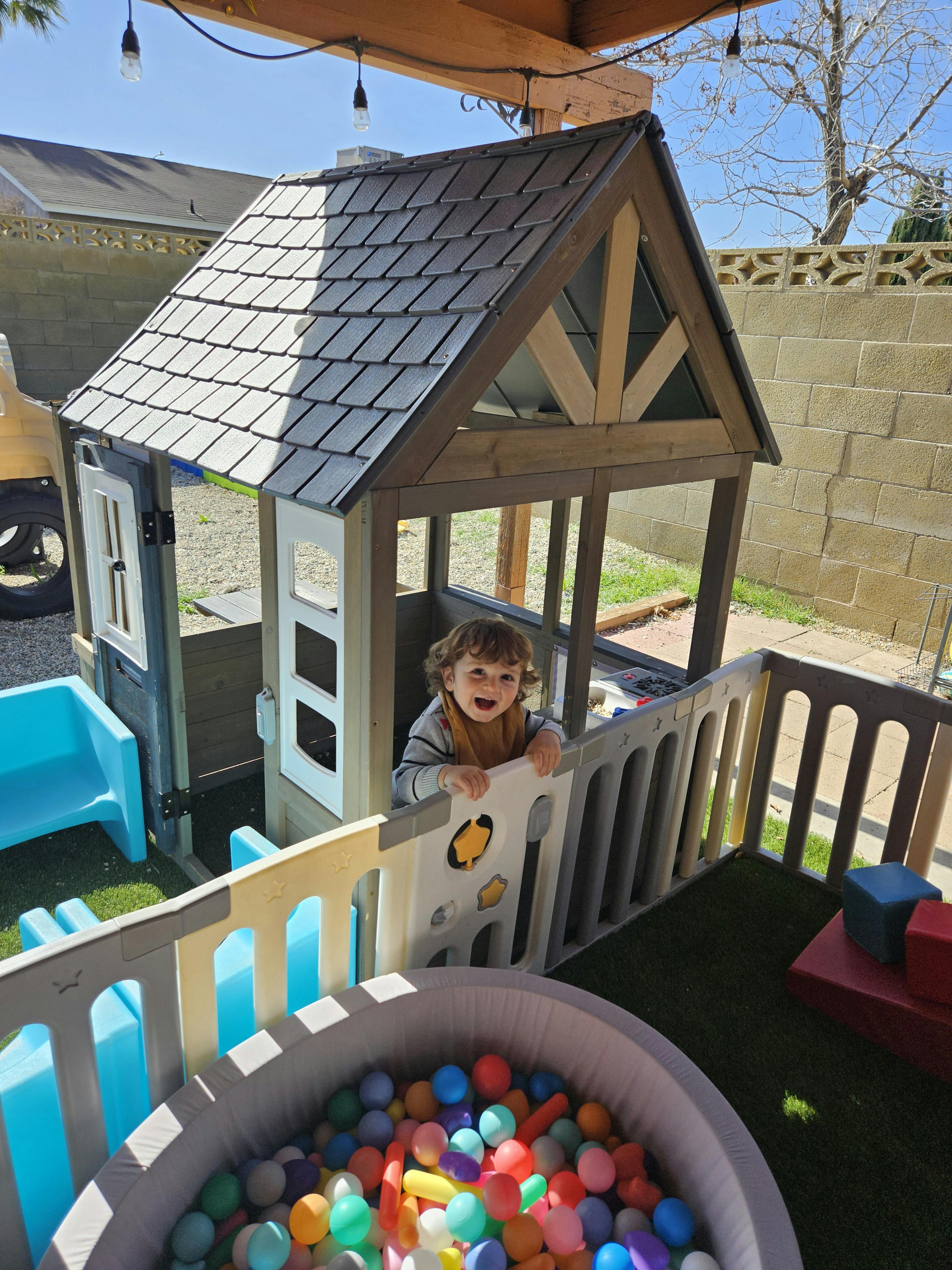 Child standing in a wooden playhouse next to a ball pit