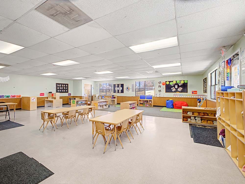 Empty classroom with small tables and chairs, shelves, and bulletin boards
