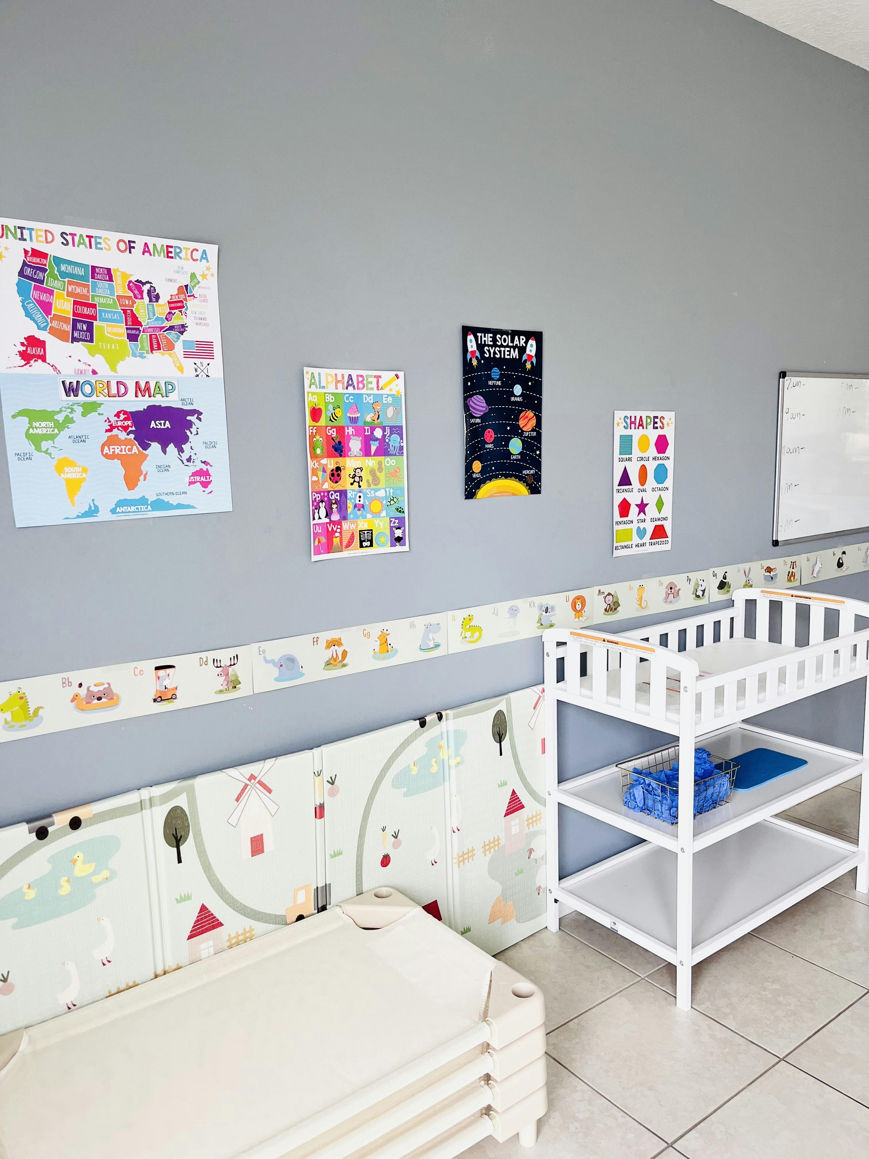 Classroom wall with educational posters, a changing table, and cots