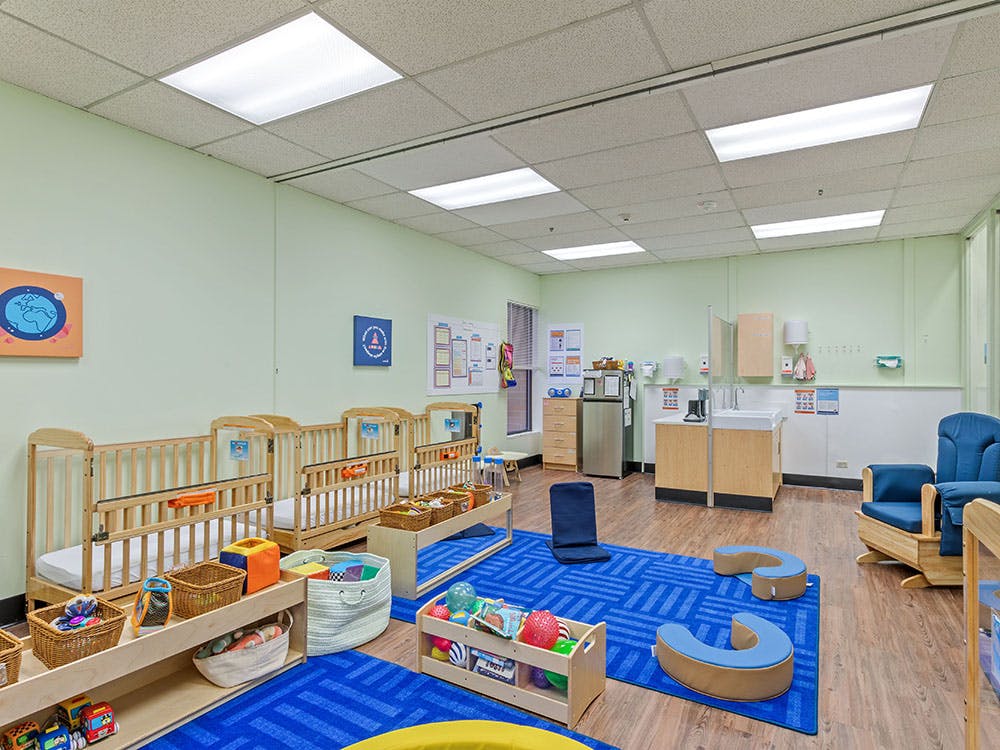 Classroom with multiple cribs, a sink area, and blue floor mats with toys