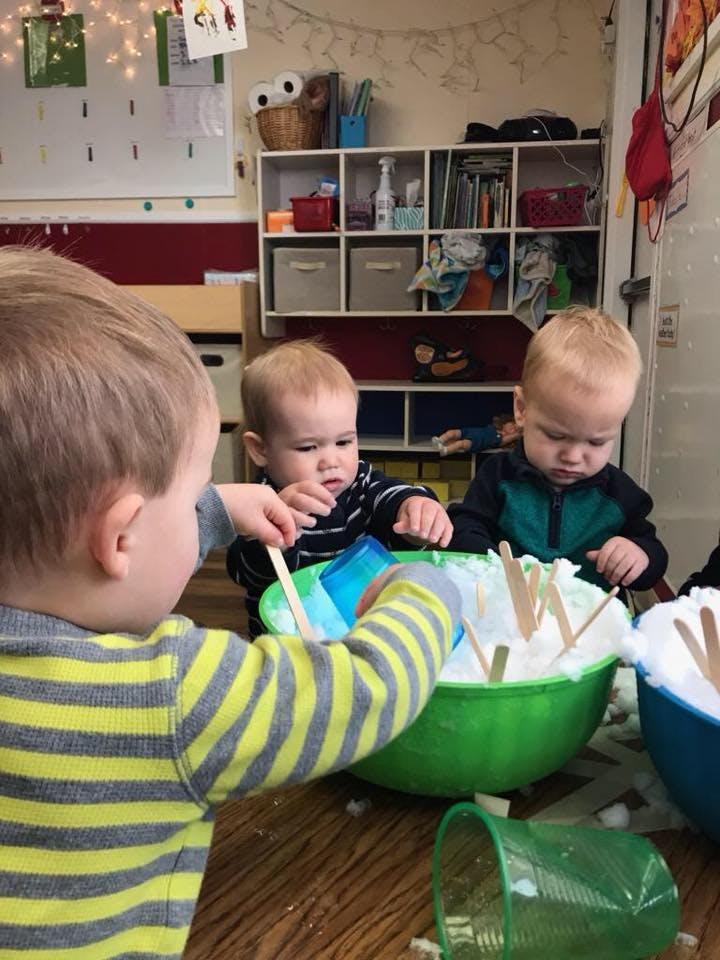 Three children playing with white foam and wooden sticks in bowls