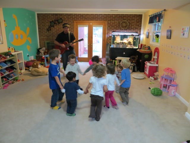 Person playing guitar for a group of children holding hands in a circle