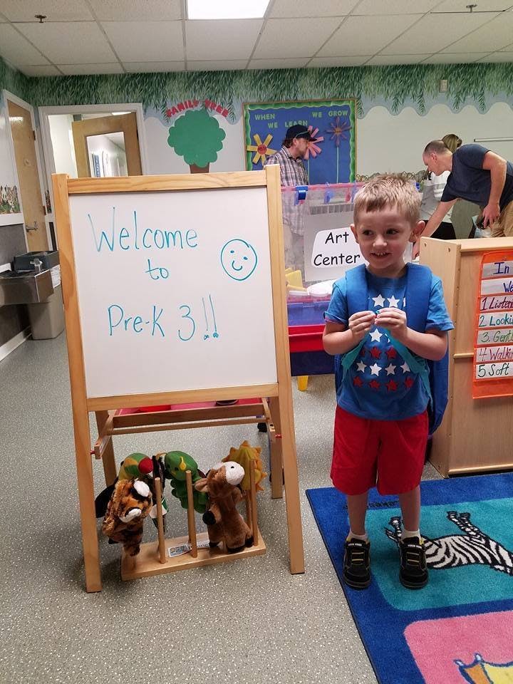 Child standing next to a whiteboard that says "Welcome to Pre-K 3!!"