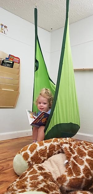 Child reading a book in a green swing chair