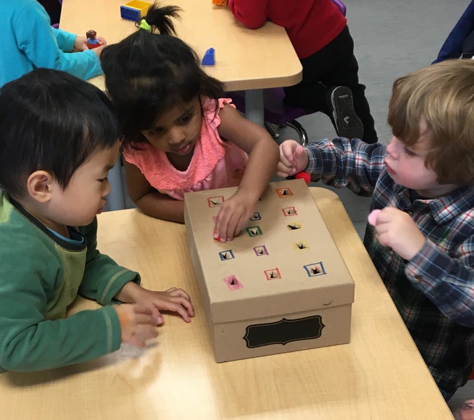 Three children playing with a box on a table