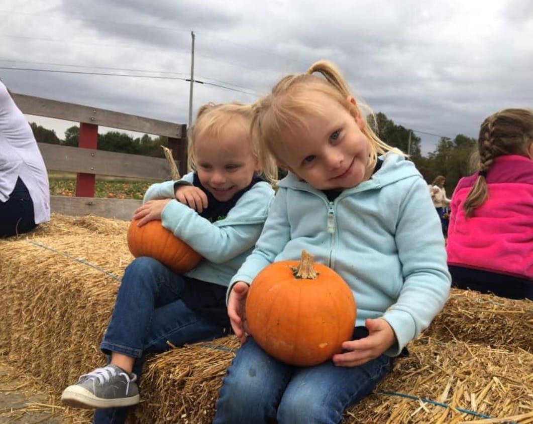 Two children sitting on hay bales holding pumpkins