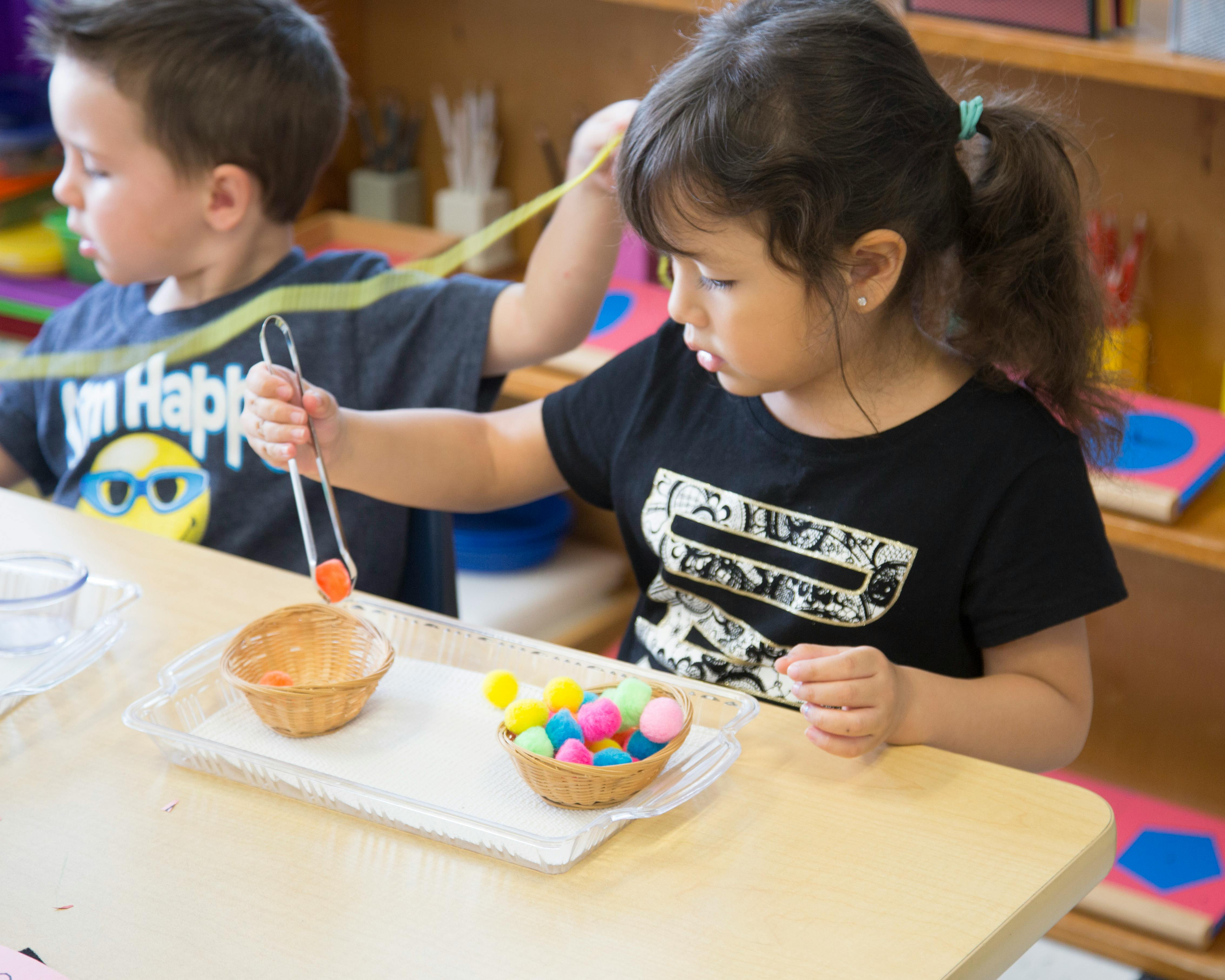 Child using tongs to move pom-poms from one bowl to another