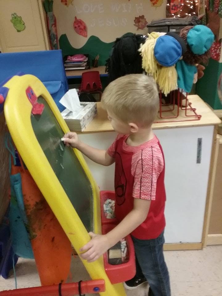 Child drawing on a yellow easel with chalk