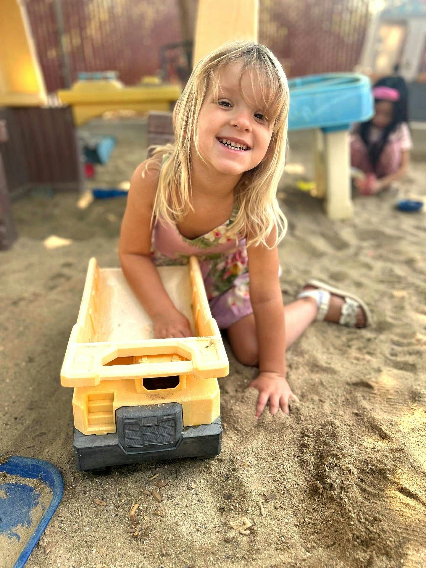 Child playing with a toy dump truck in a sandbox