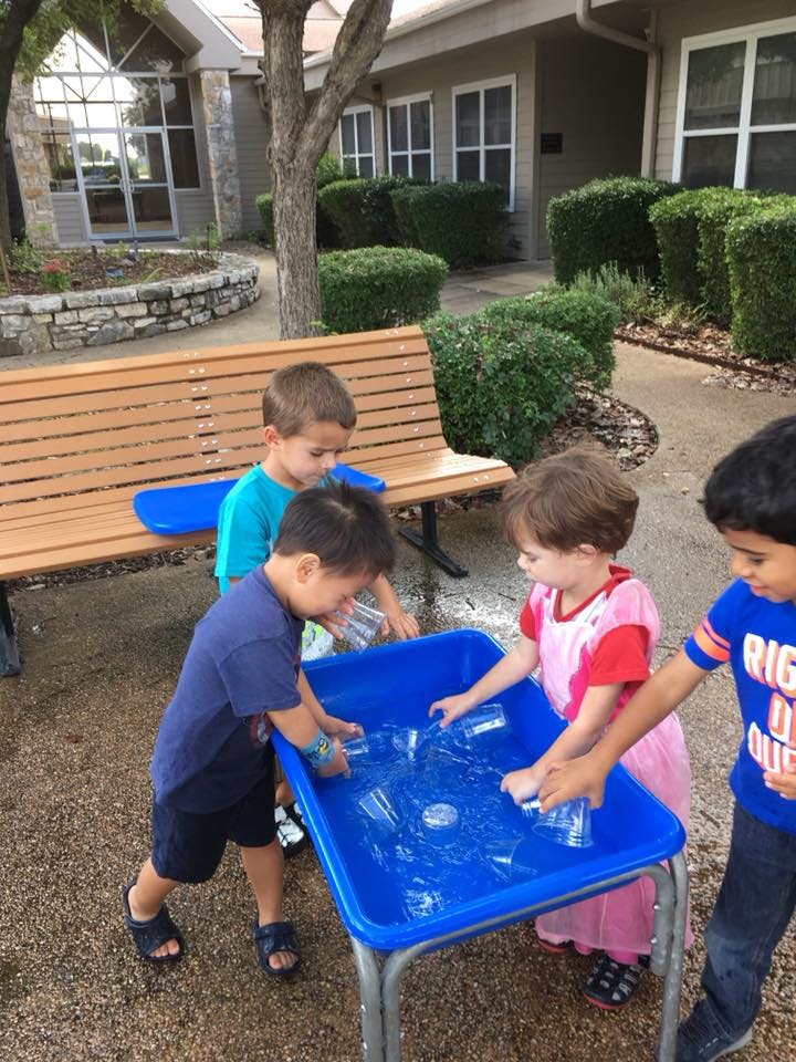 Children playing with water in a blue bin outdoors