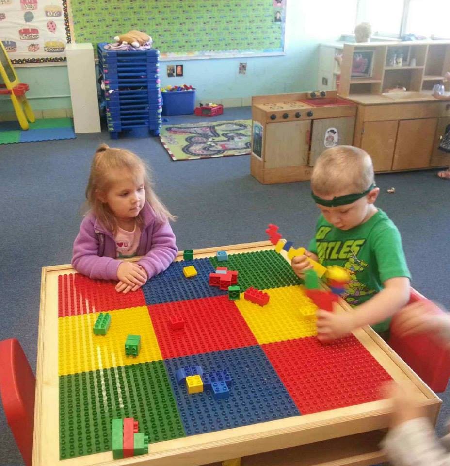 Two children playing with building blocks at a table in a classroom
