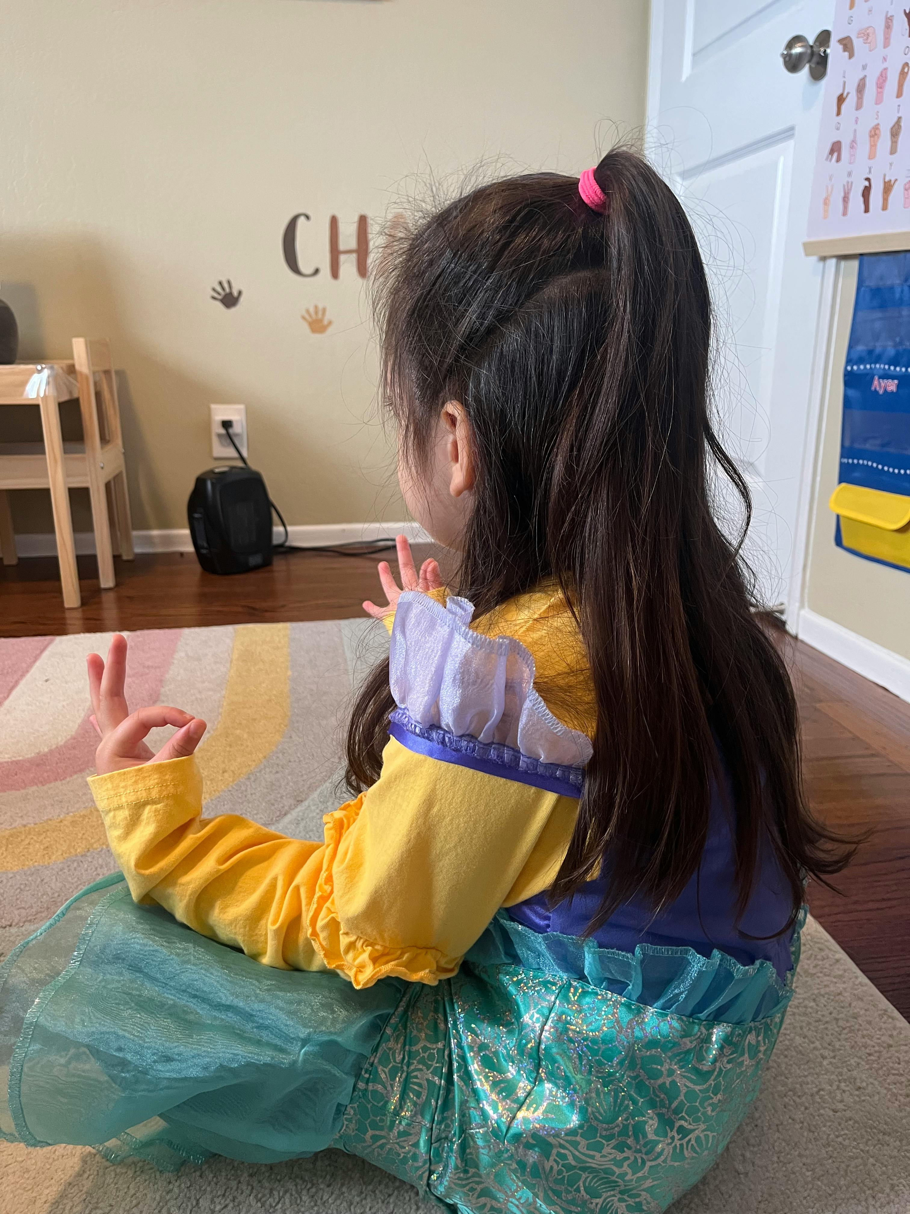Child in costume sitting on a rug with hands in a gesture