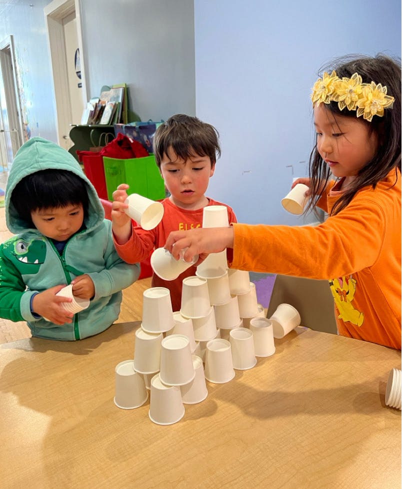 Three children stacking white cups into a pyramid