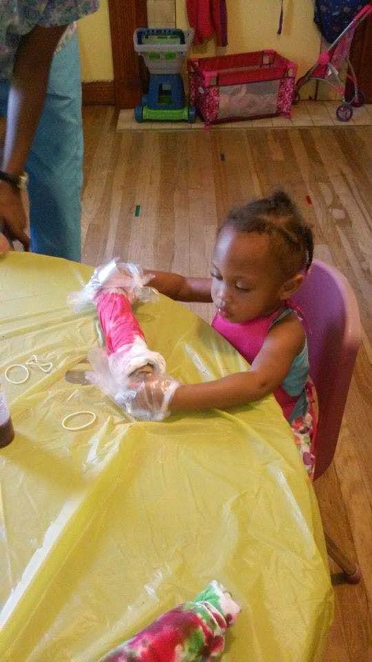 Child wearing gloves and holding a tie-dye shirt over a yellow table covering
