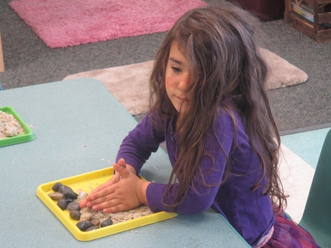 Child playing with sand and rocks on a yellow tray