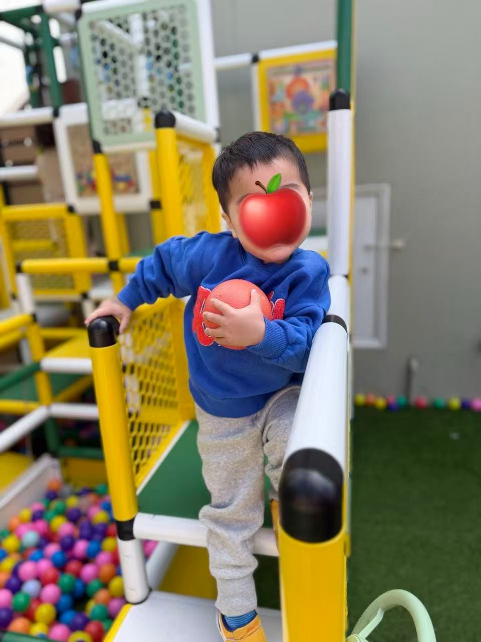 Child holding a ball while standing on indoor playground equipment