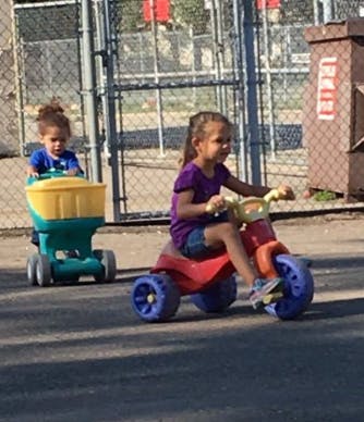 Child riding a tricycle and another child in a toy wagon