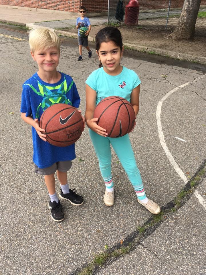 Two children holding basketballs on a paved surface