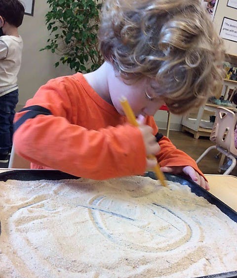 Child drawing in sand with a stick