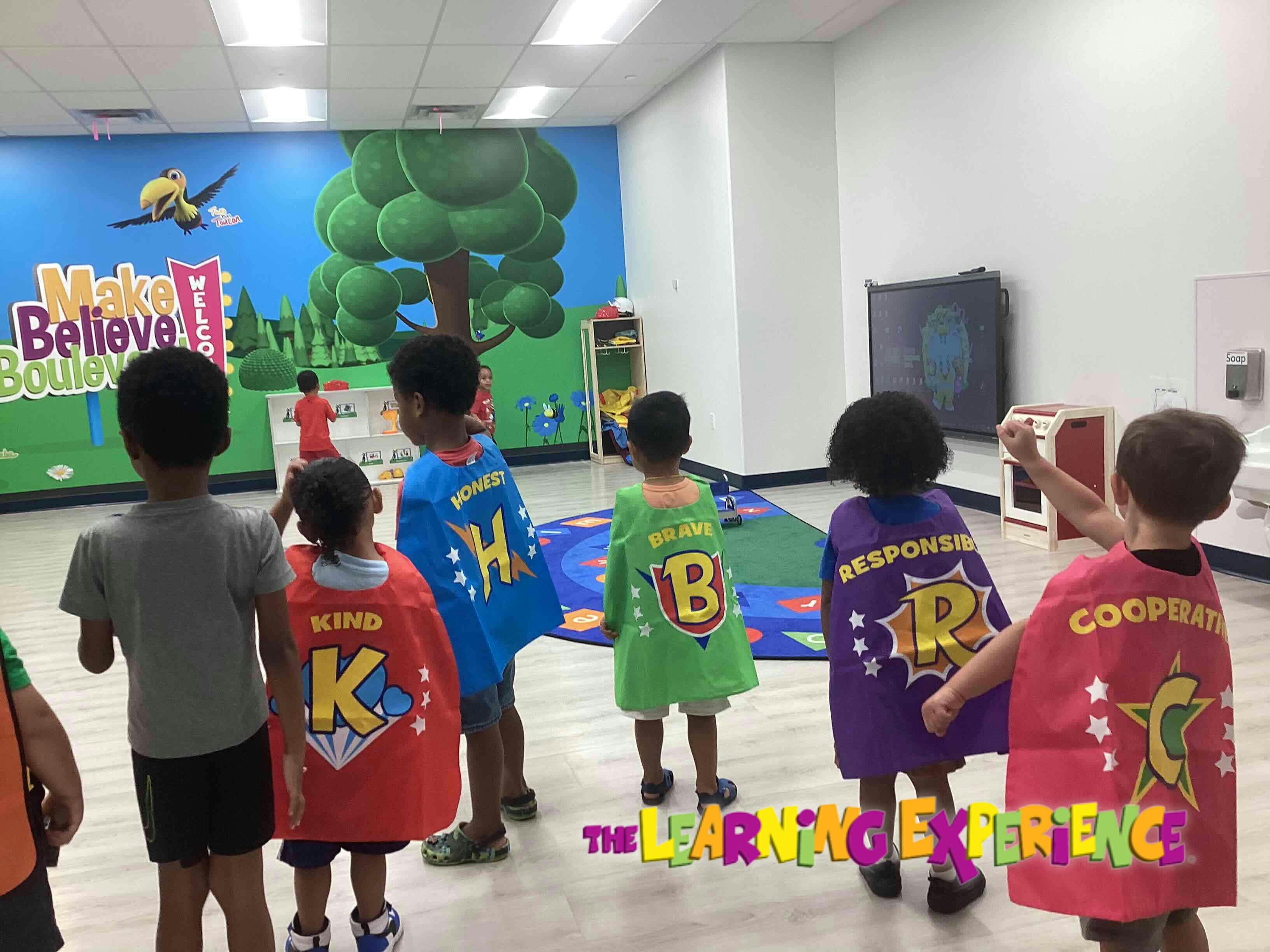 Children wearing superhero capes in a room with a colorful mural