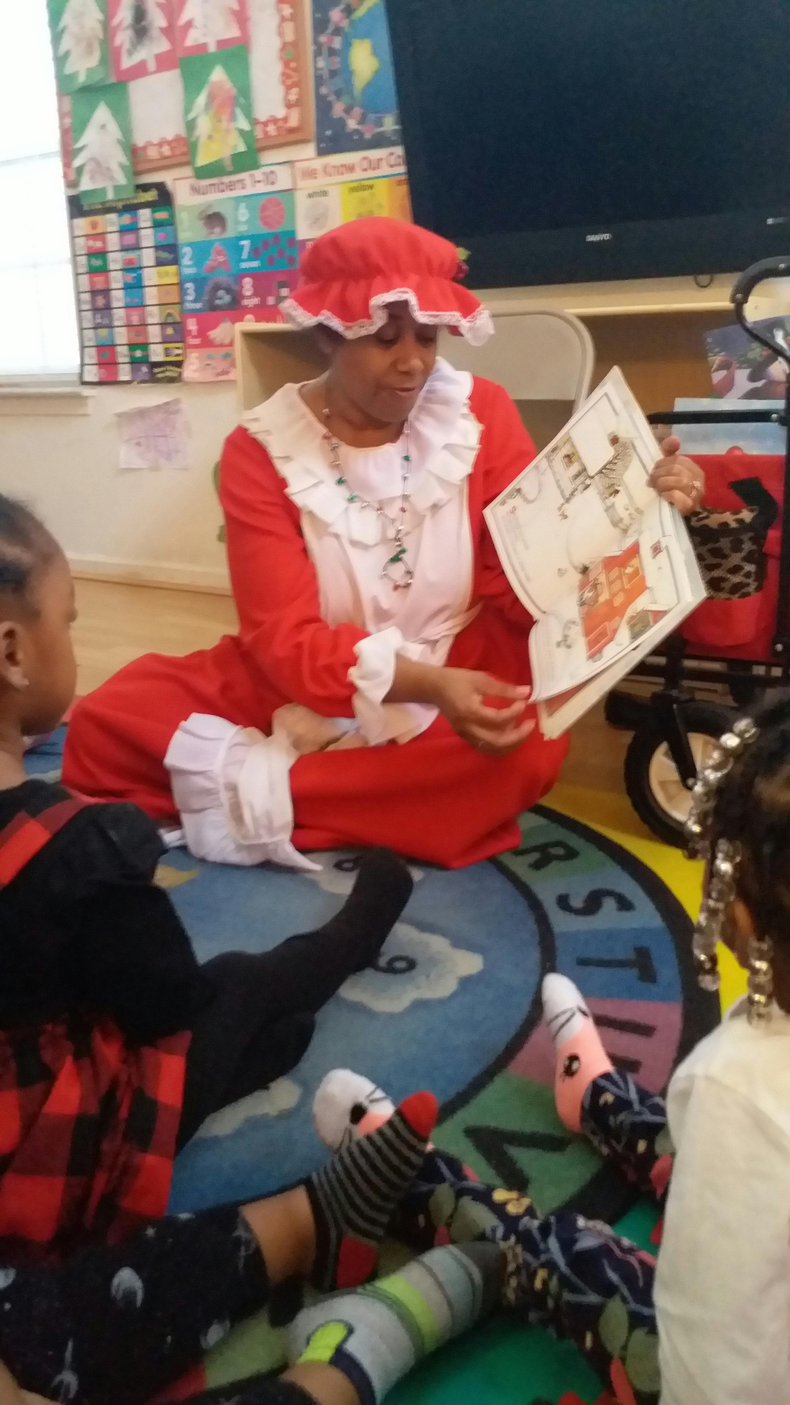 Person in red costume reading a book to children in a classroom