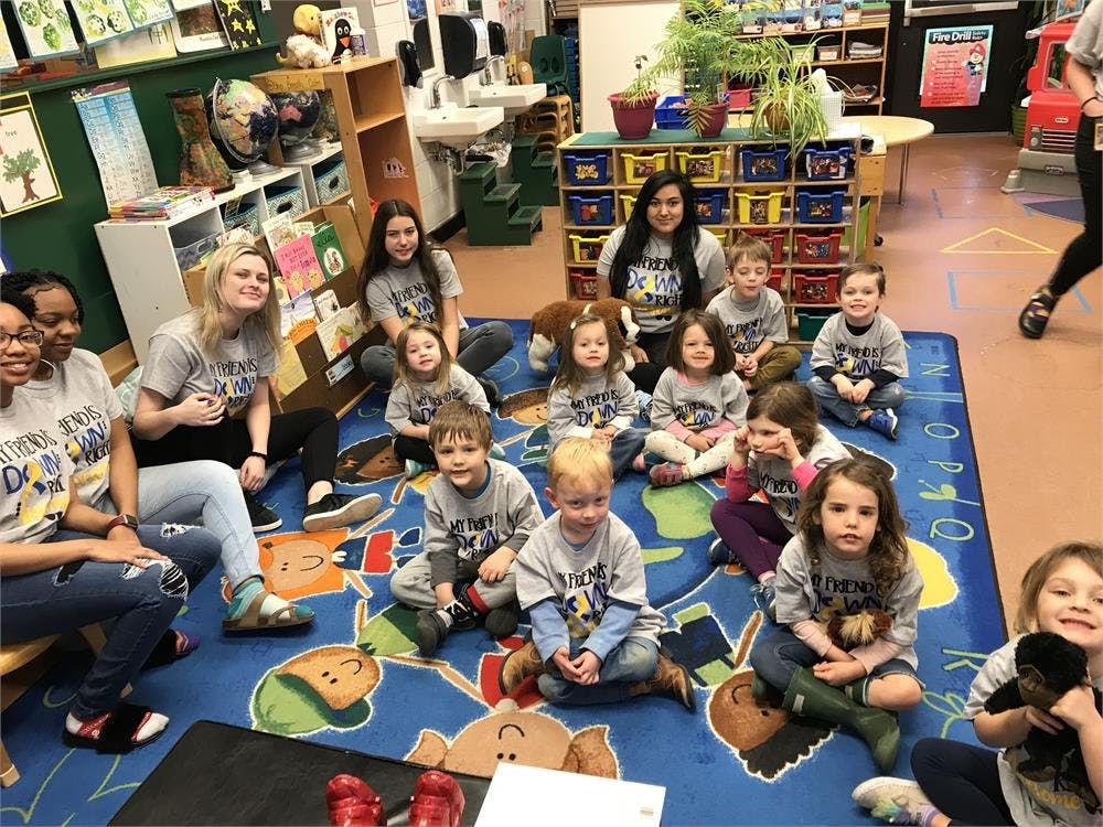 Group of adults and children sitting on a rug in a classroom