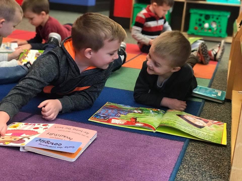 Two children lying on the floor looking at books in a classroom