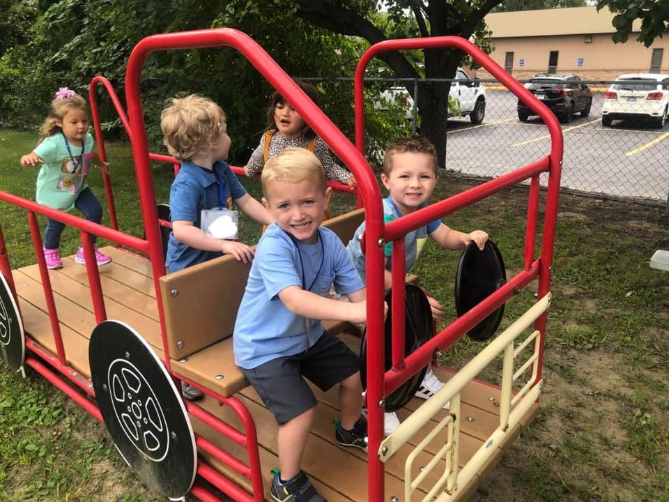 Children playing on a red and brown playground structure shaped like a vehicle