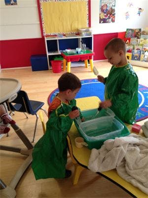 Two children in smocks playing with water at a table in a classroom