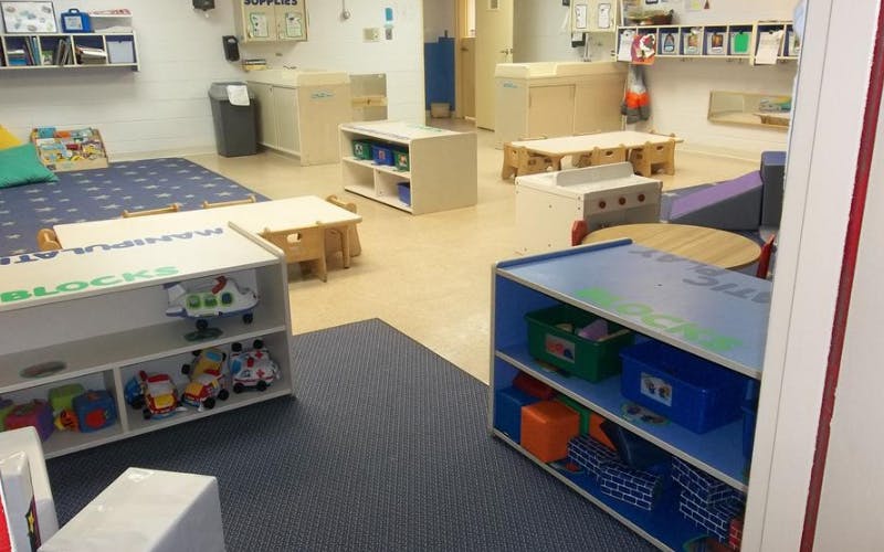 An empty childcare room with tables, toy shelves, and changing stations