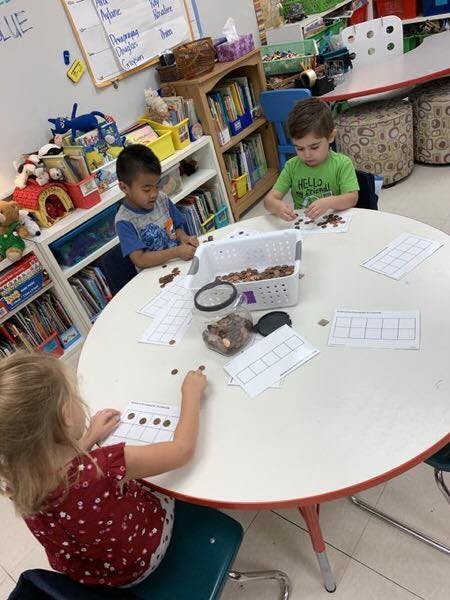 Three children at a table working with small objects and papers in a classroom