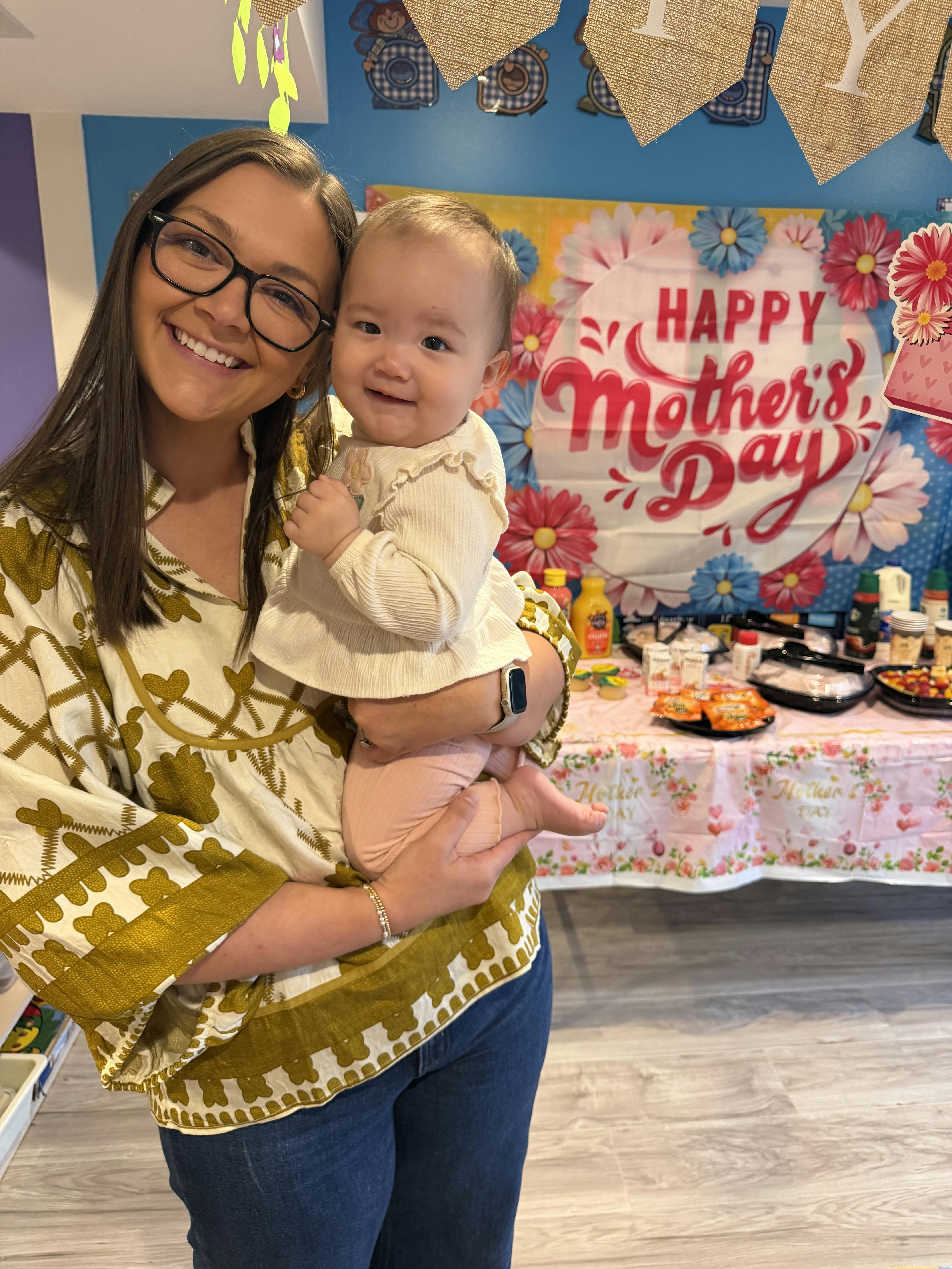 Smiling person in glasses holding a baby in a decorated room