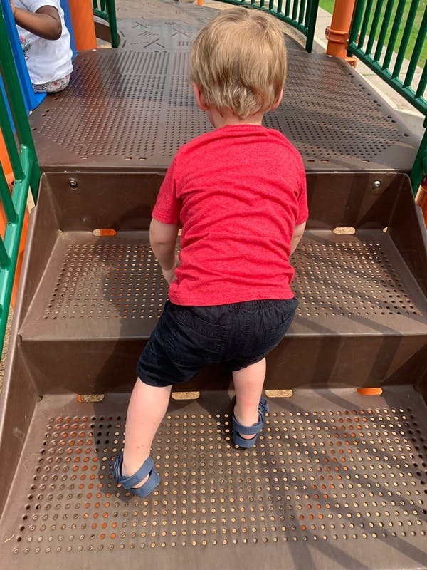Child in red shirt and black shorts climbing stairs on a playground