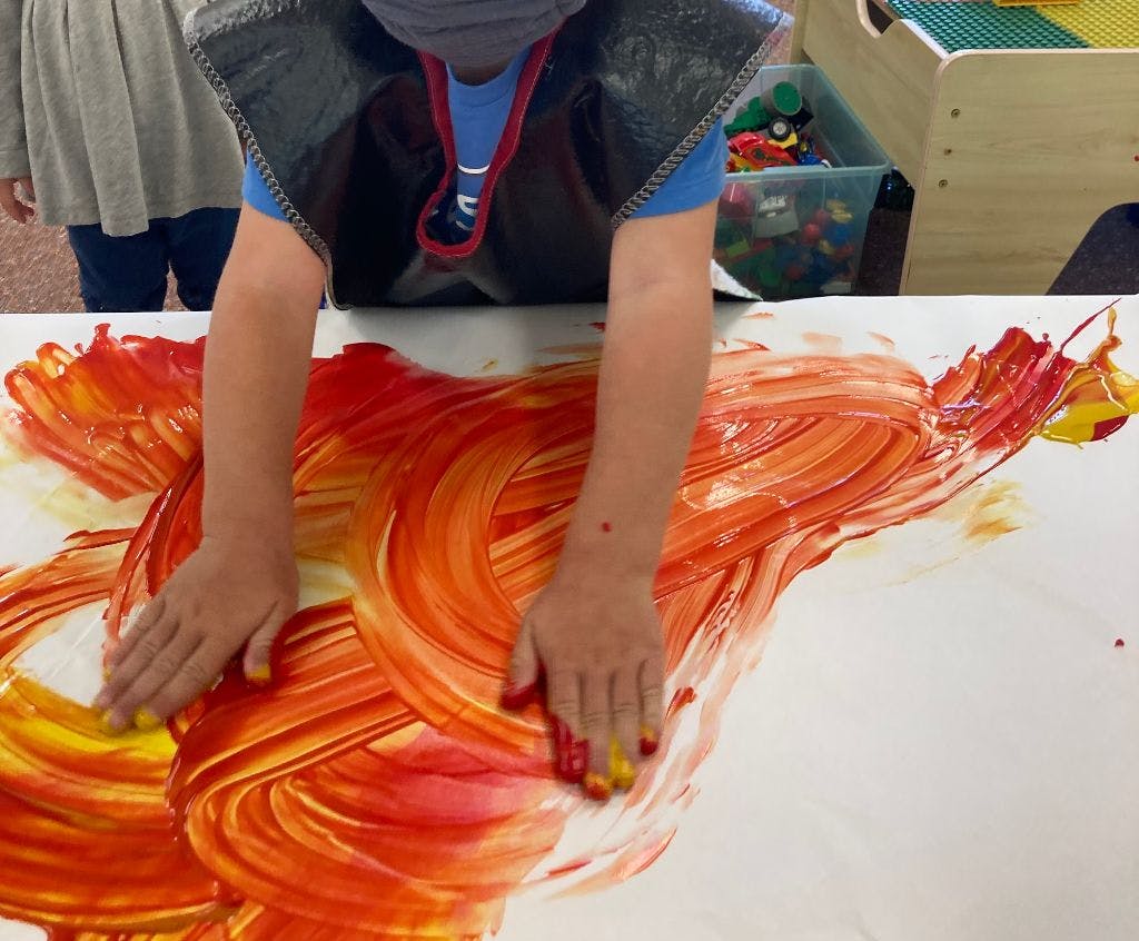 Child finger painting with red and yellow paint on a large white sheet