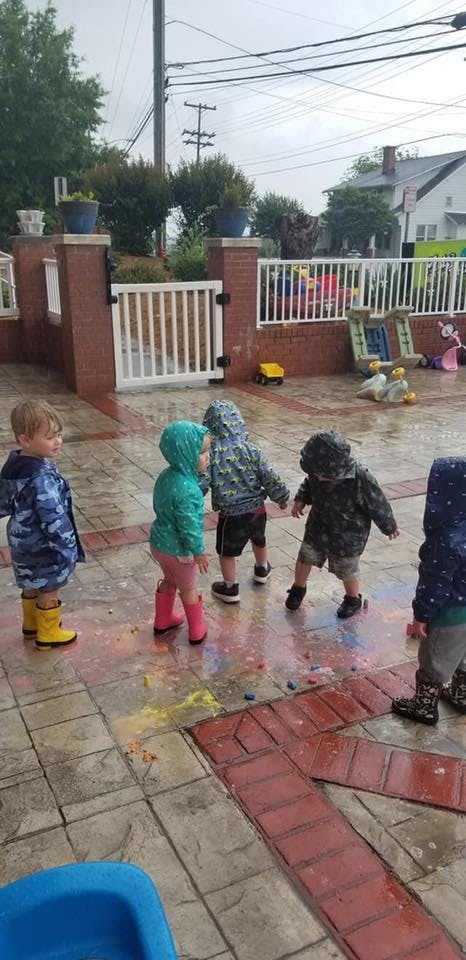 Children in raincoats and boots playing on a wet patio