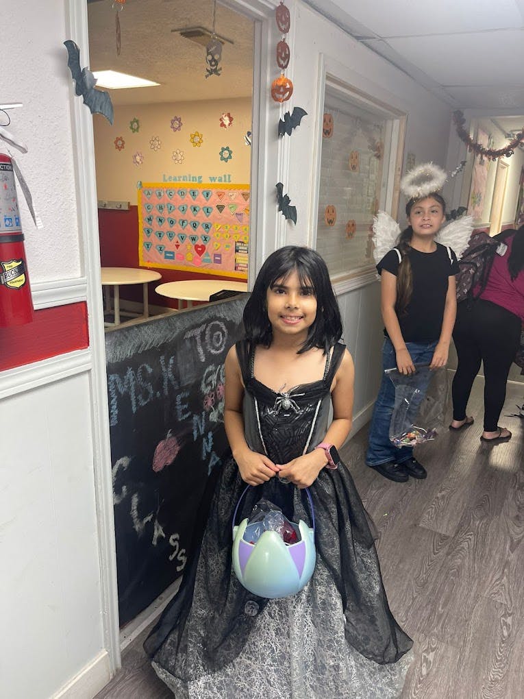 Child in a dark costume holding a candy bucket, another child in an angel costume