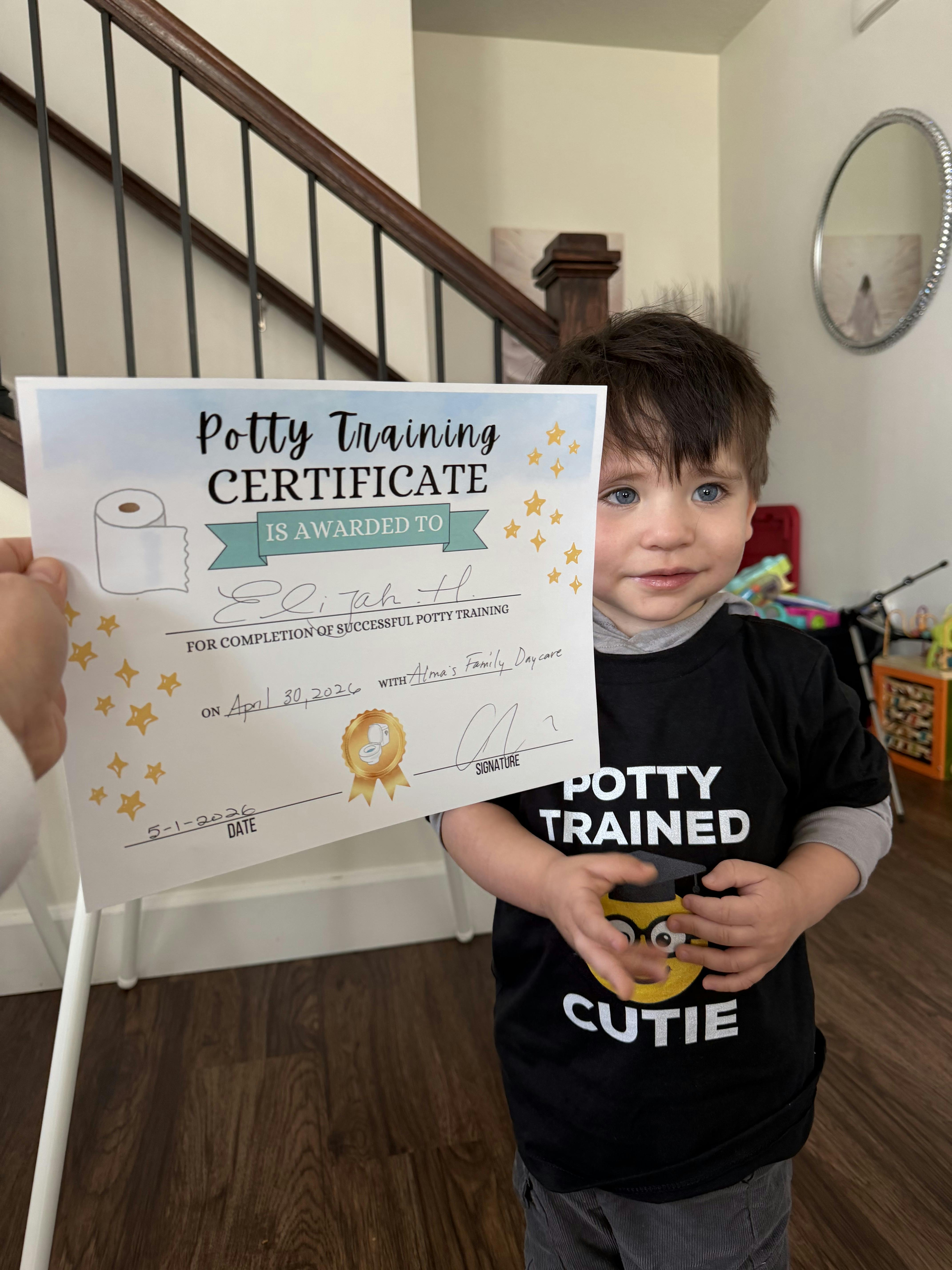 Child wearing a Potty Trained Cutie shirt holding a potty training certificate