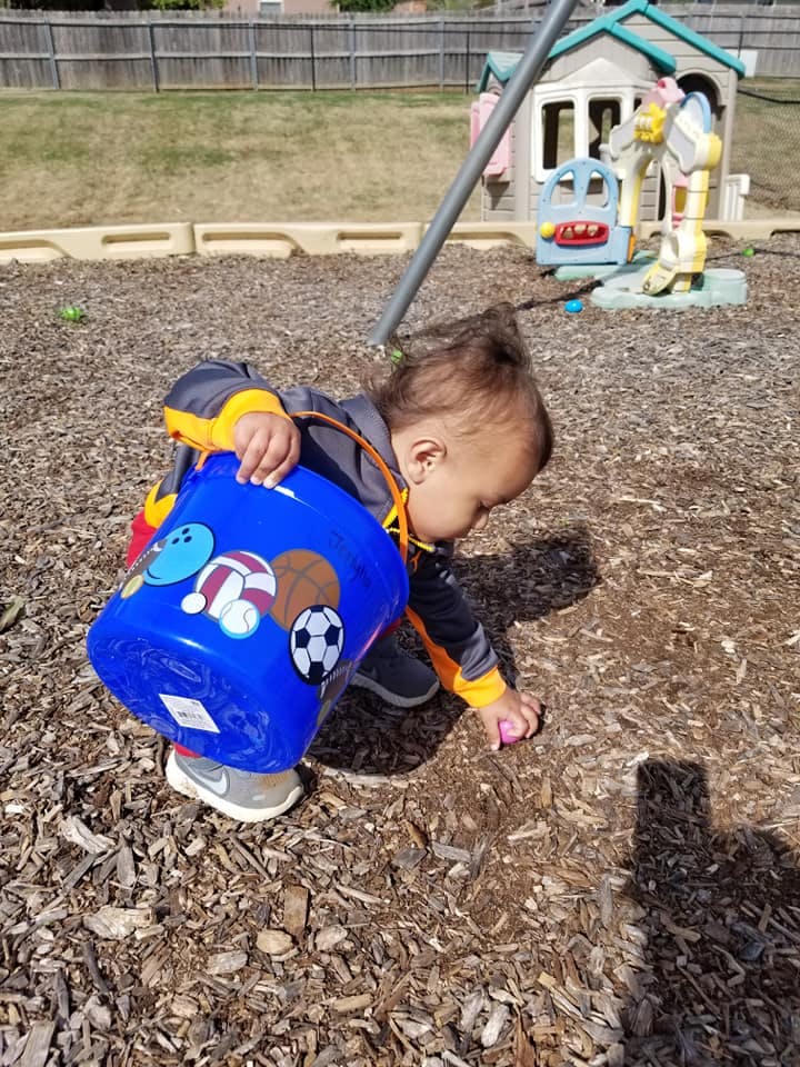 Child holding a blue bucket and picking up an object from the ground