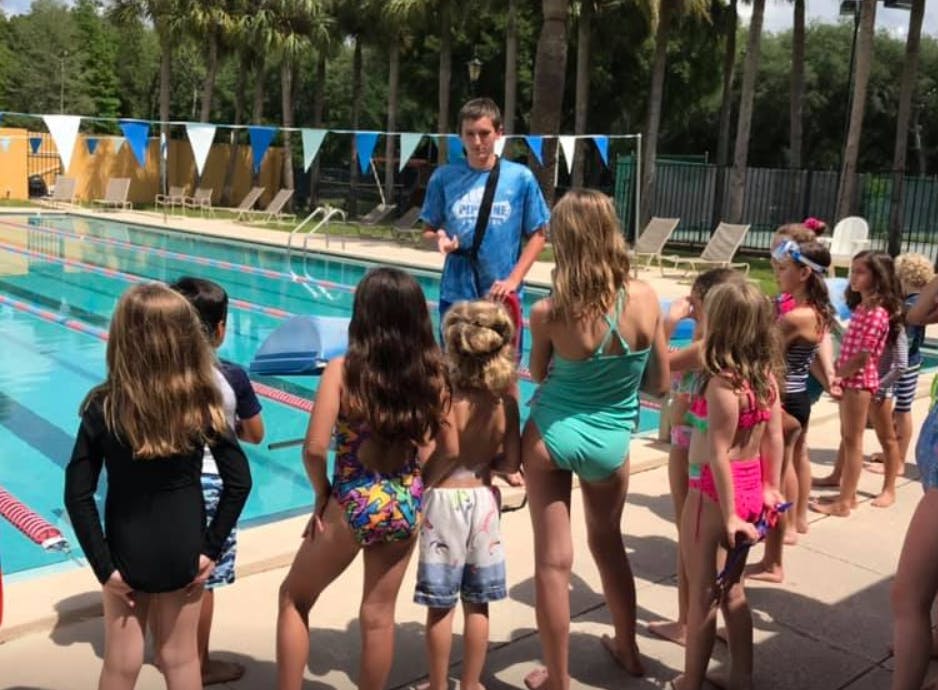 Adult person talking to a group of children in swimsuits by a pool