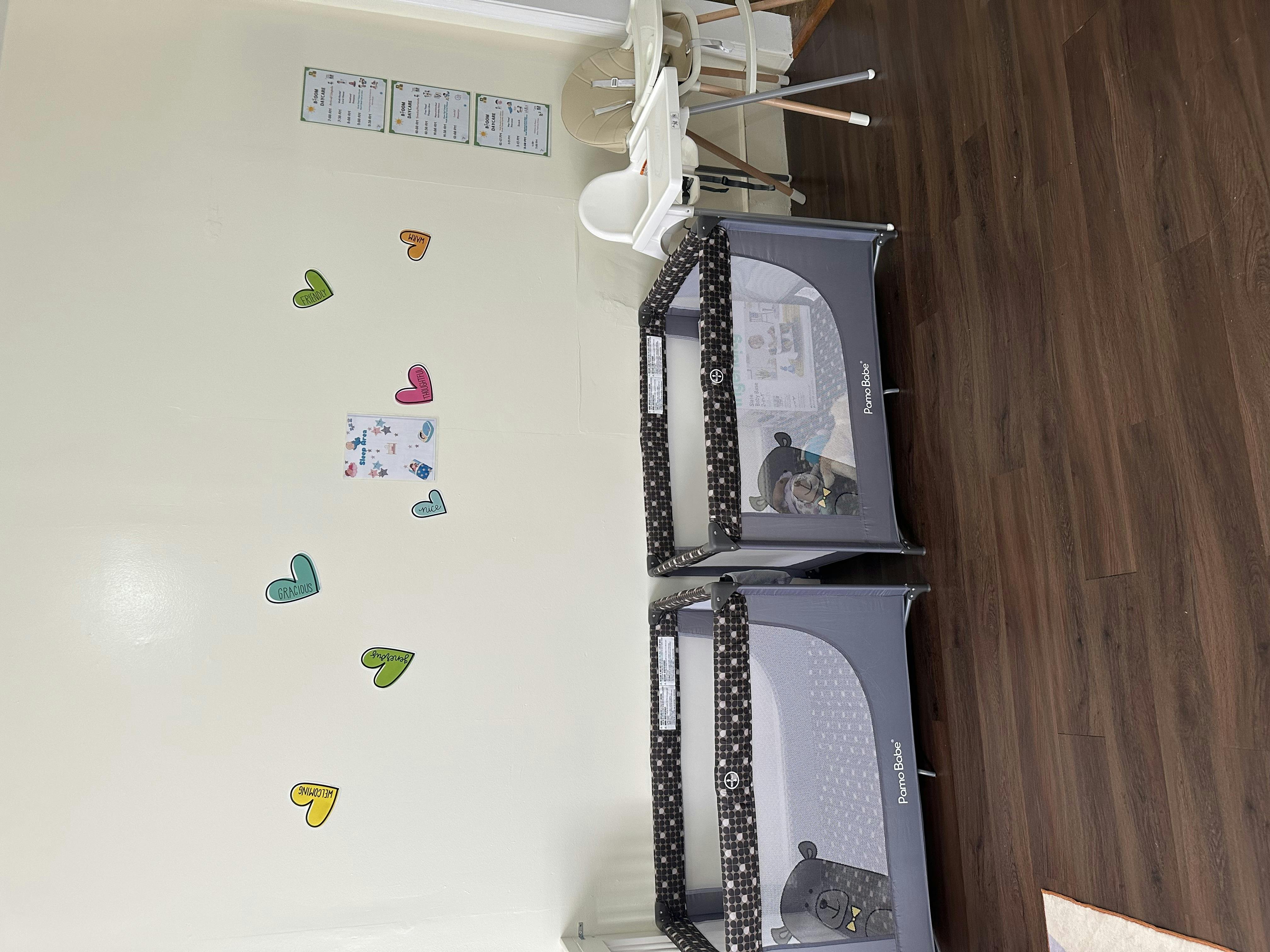 Two portable cribs with a child in each, next to a wall with heart decorations