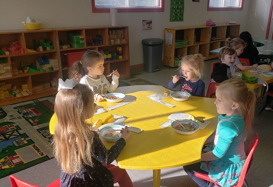 Children eating at a yellow table in a classroom